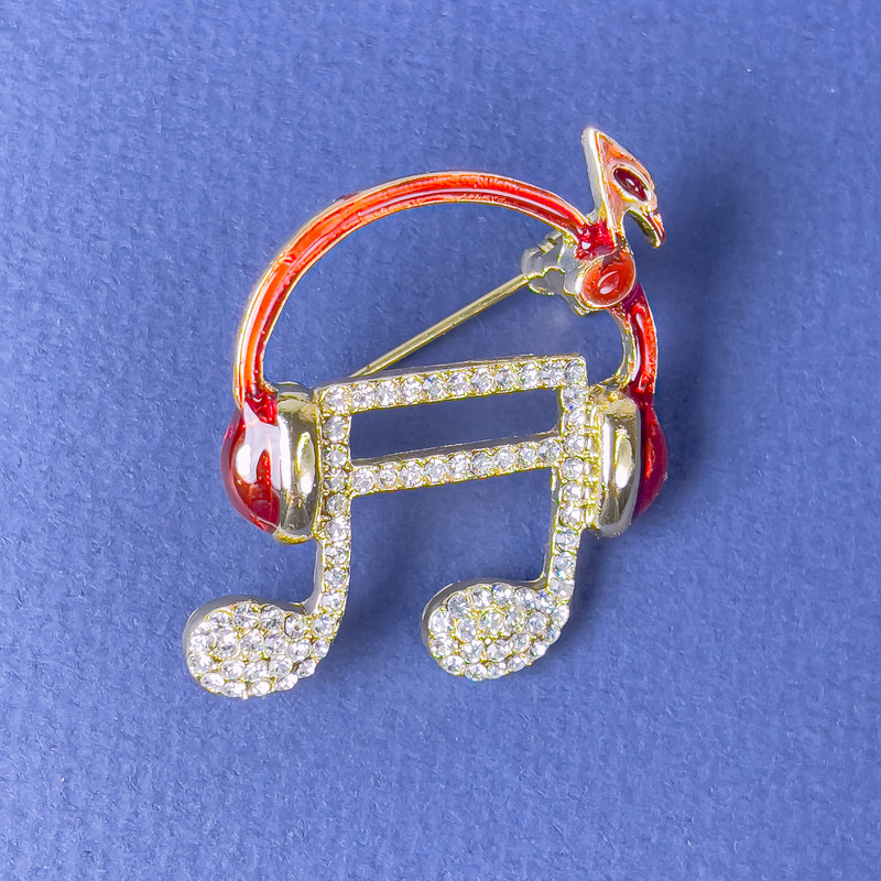 Brosche 'Note im Kopfhörer' – weiße Strasssteine, rote Emaille, goldfarbenes Metall, 27×32 mm+