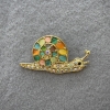 Schneckenbrosche mit buntem Katzenauge und Strasssteinen, hellgoldenes Metall, 28 × 55 mm