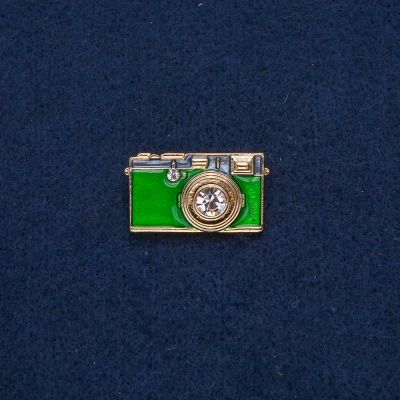 Брошка Фотоапарат золотистий метал із зеленою емаллю і білими каменями 30х17 мм + -